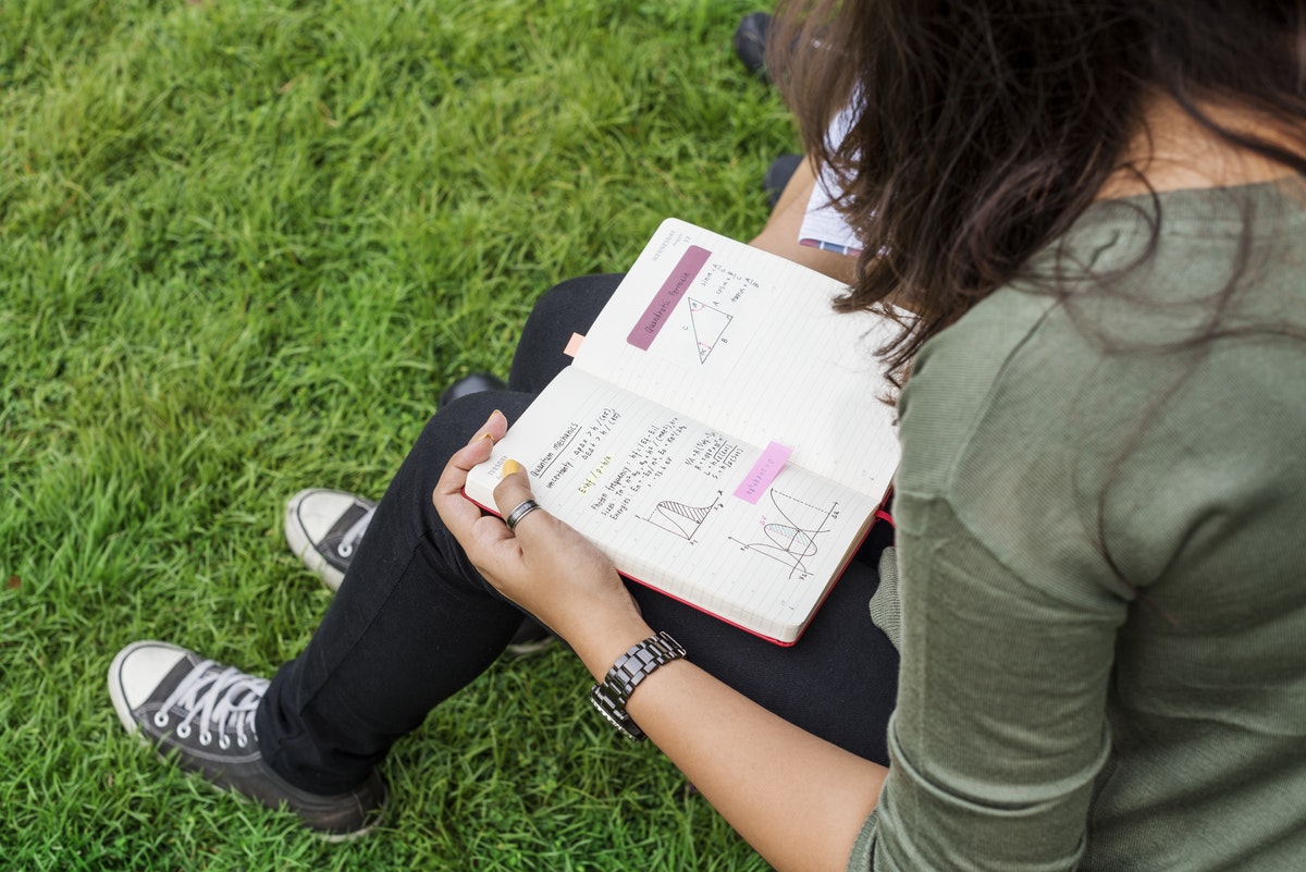 jeune femme travaillant ses devoirs dehors dans l'herbe